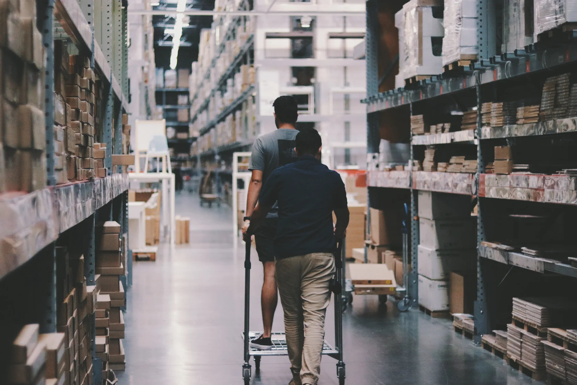 Warehouse workers moving a trolley between storage aisles
